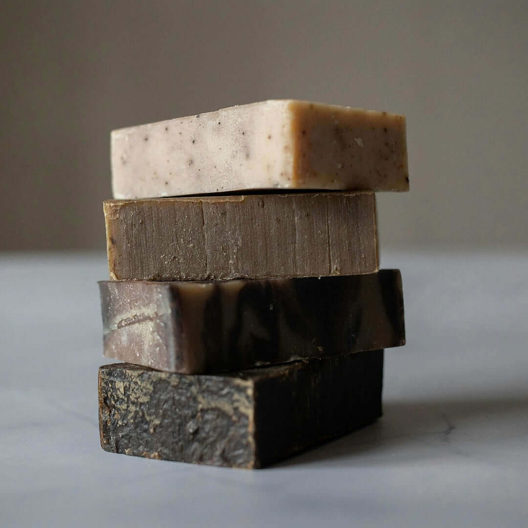 Stack of three different types of soap on a neutral background
