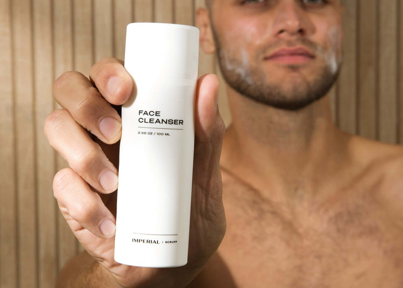 Man holding a bottle of face cleanser labeled 'Imperial Scruff' against a neutral background