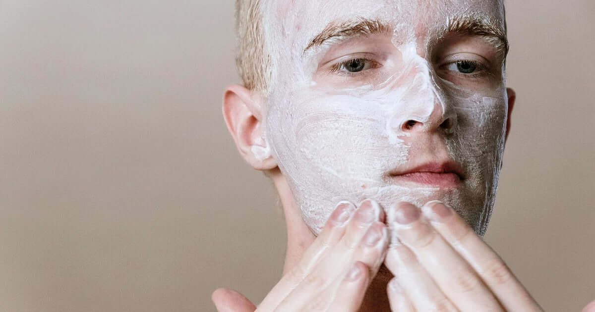 Man applying a white facial mask to his face against a neutral background