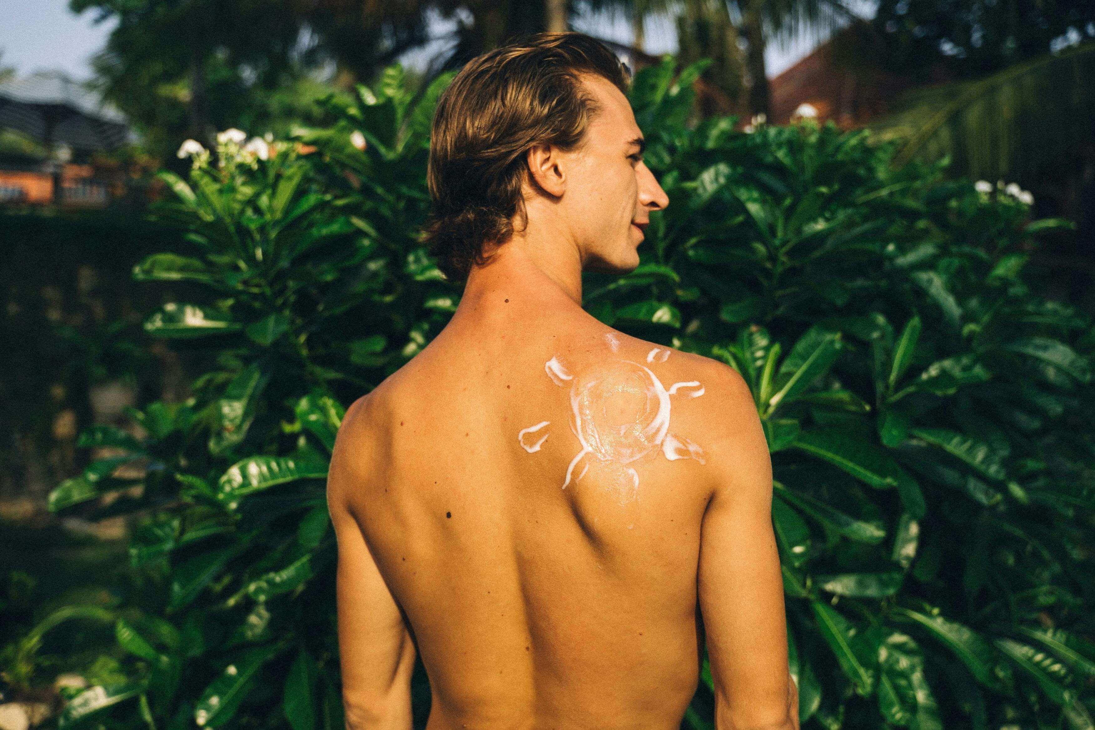 Man with sunscreen on his back standing in a tropical setting