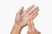 Hand applying a small amount of beard balm to another hand on a white background