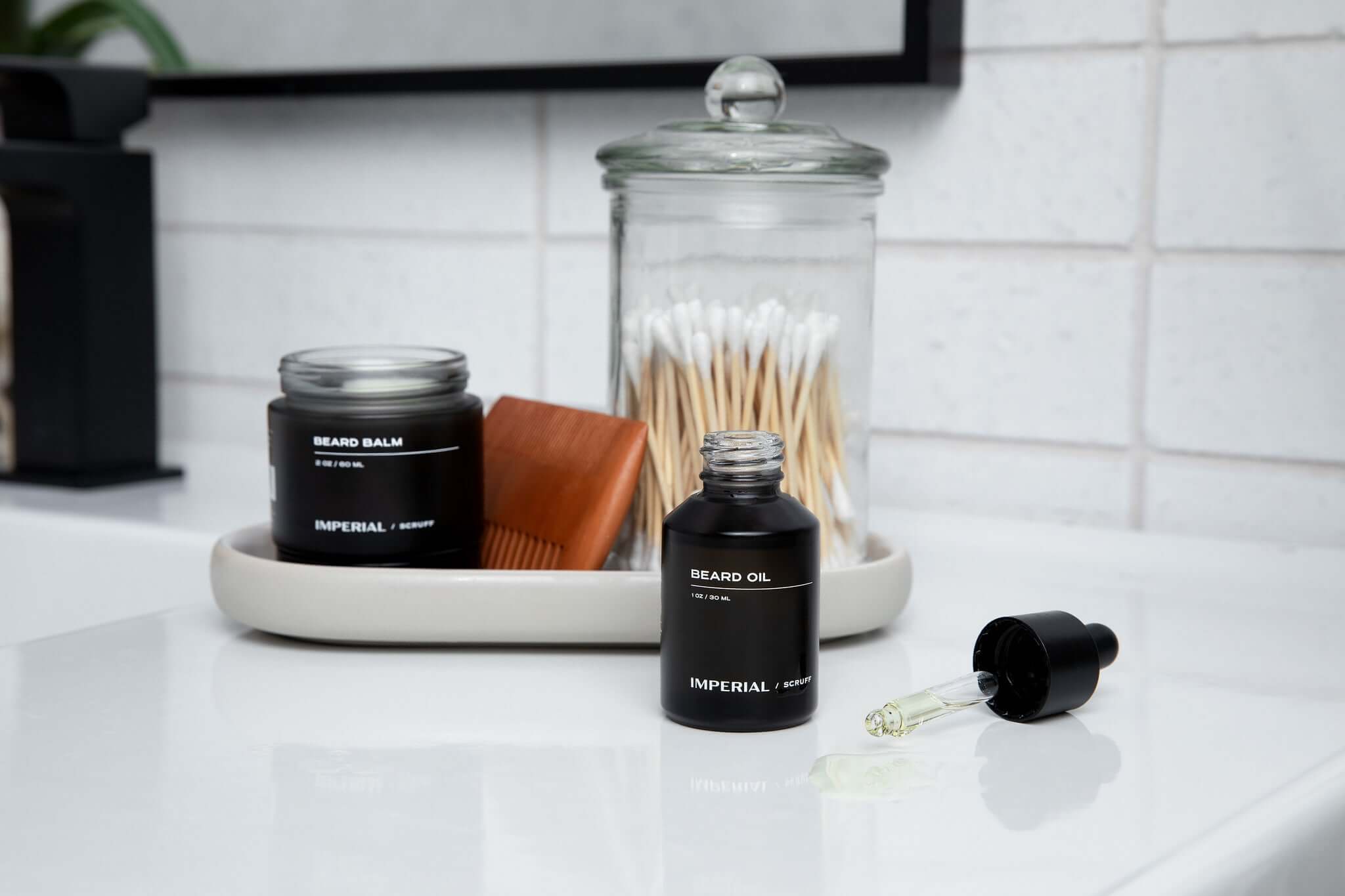 Beard care products including balm, oil, and a dropper on a bathroom counter.