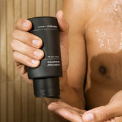 Person holding a black shampoo bottle with a blurred background.