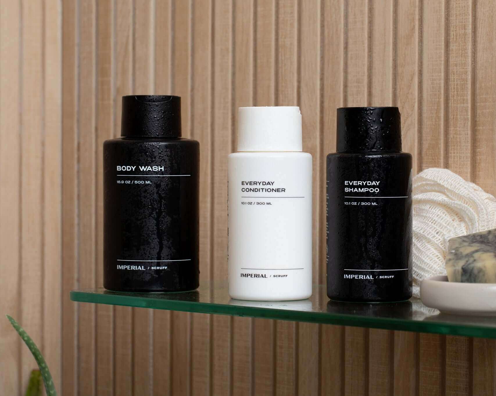 Three bottles of Imperial Scruff hair and body care products on a glass shelf with a wooden background.