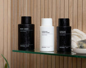 Three bottles of Imperial Scruff hair and body care products on a glass shelf with a wooden background.