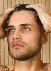 Man washing his hair with shampoo in a shower setting